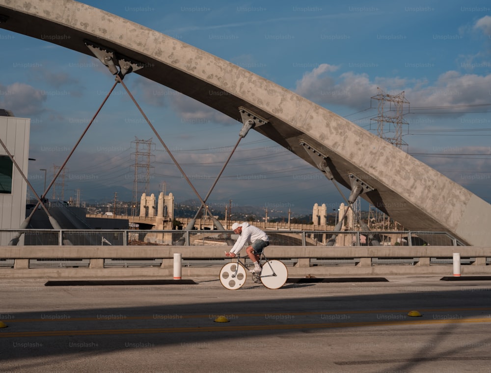 a man riding a bike down a street under a bridge