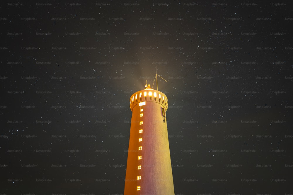 a light house lit up at night with stars in the sky