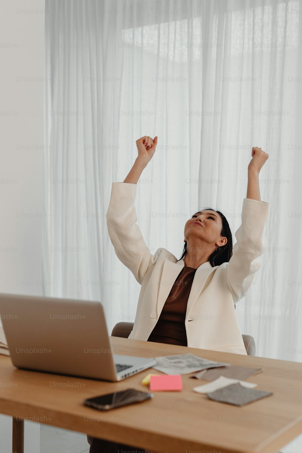 a woman sitting at a desk raising her arms in the air