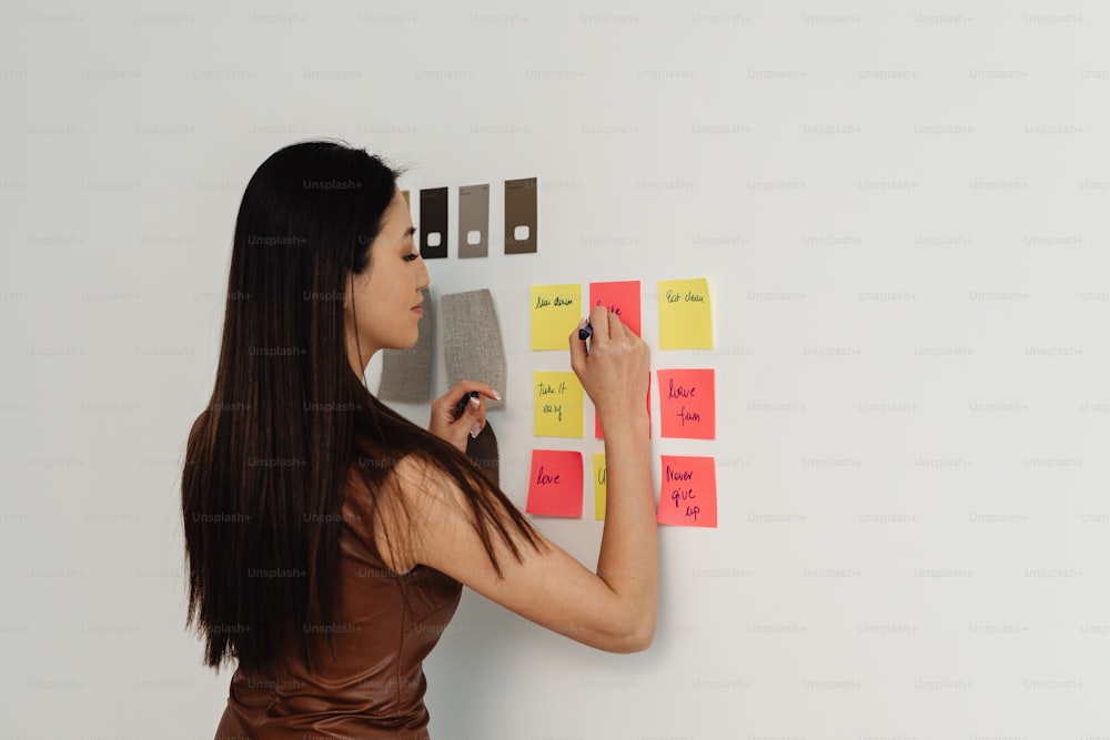 a woman writing on a wall with sticky notes