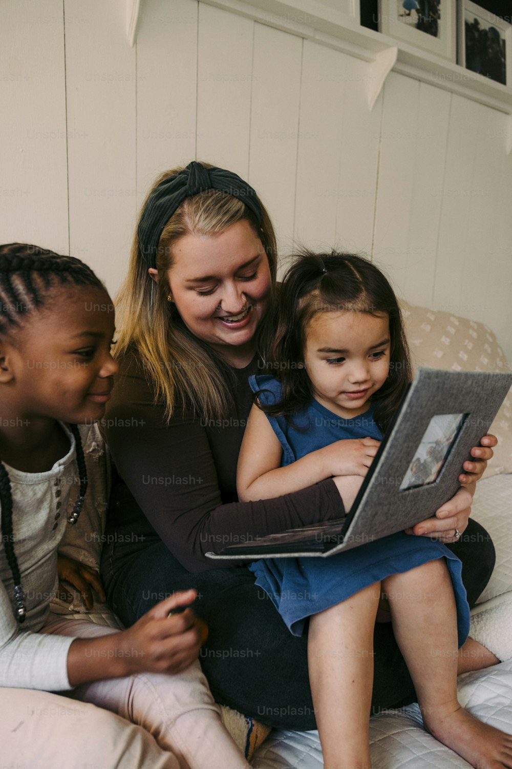 a woman and two children sitting on a bed looking at a laptop