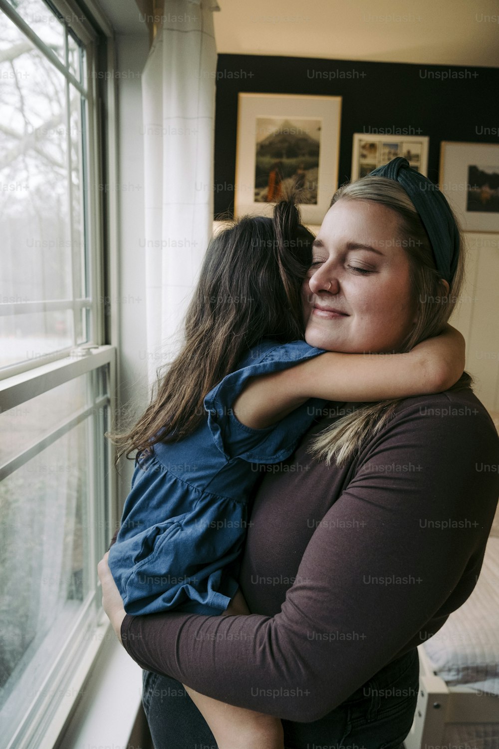 Eine Frau umarmt ein junges Mädchen vor einem Fenster