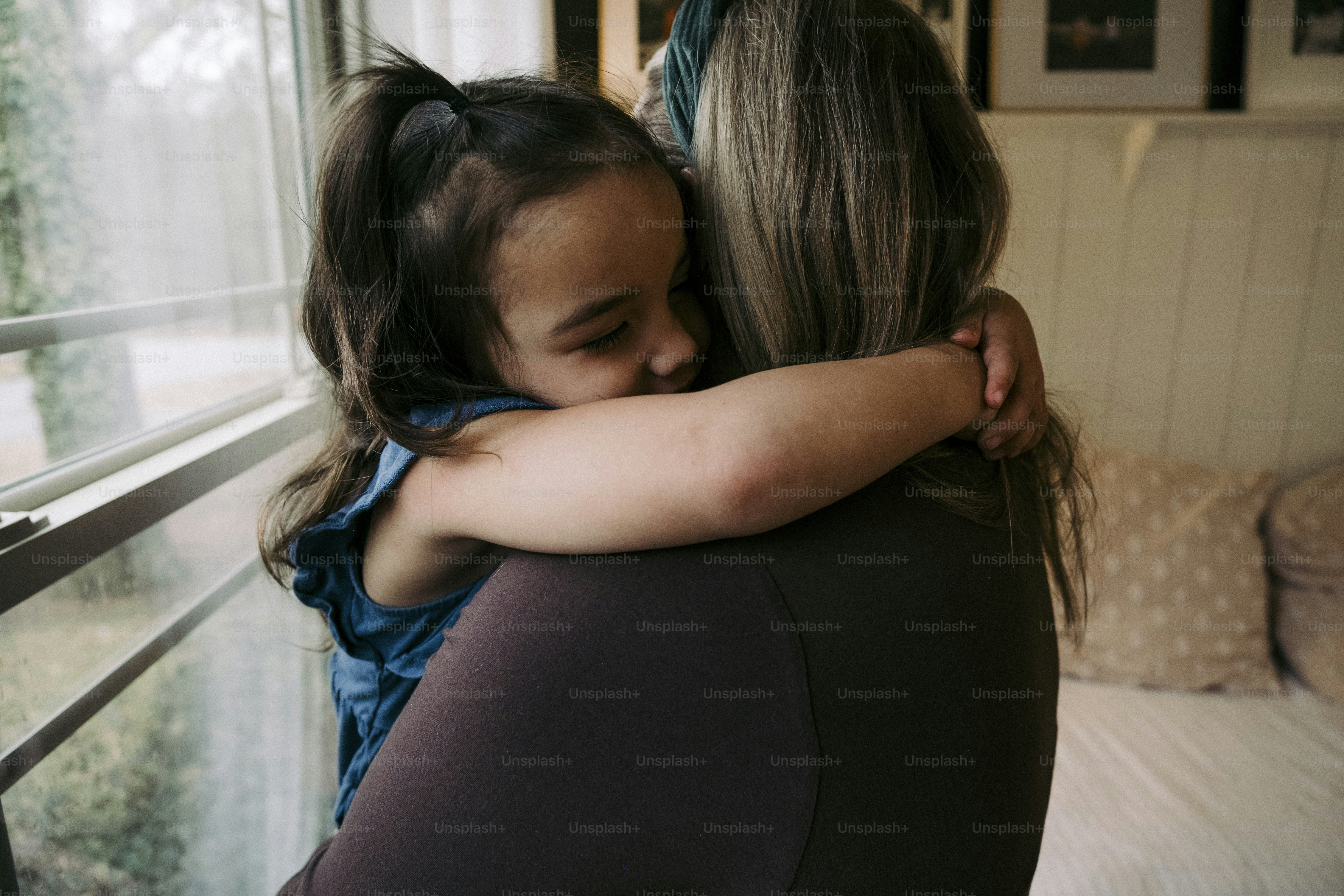 a woman hugging a little girl in front of a window