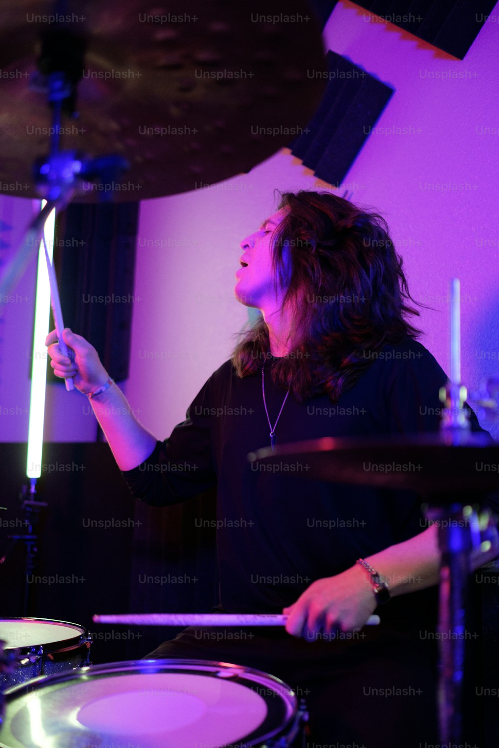 Un homme aux cheveux longs jouant de la batterie dans une pièce