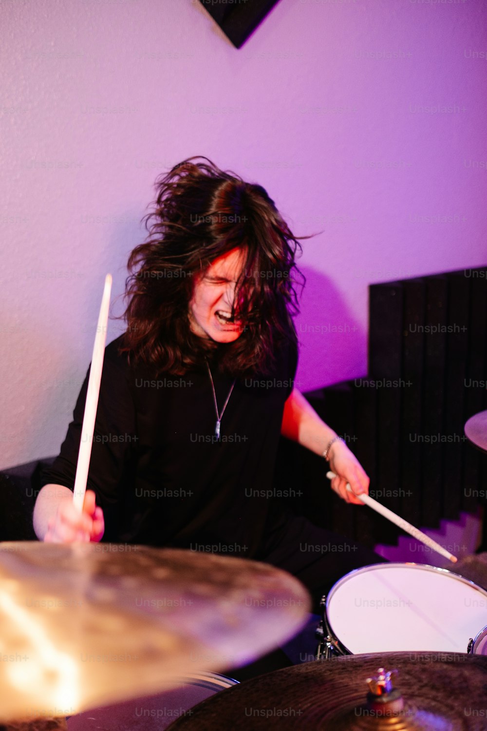 um homem com cabelos compridos tocando bateria em uma sala