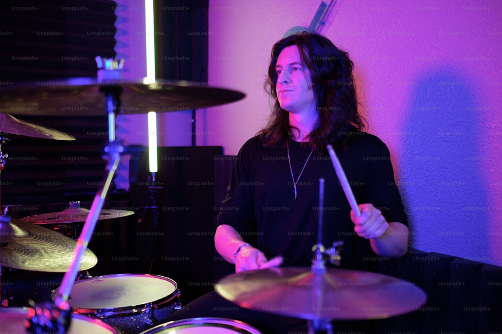 a man with long hair playing drums in a room
