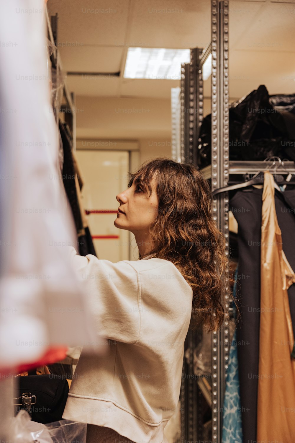 a woman in a white top is looking at a rack of clothes
