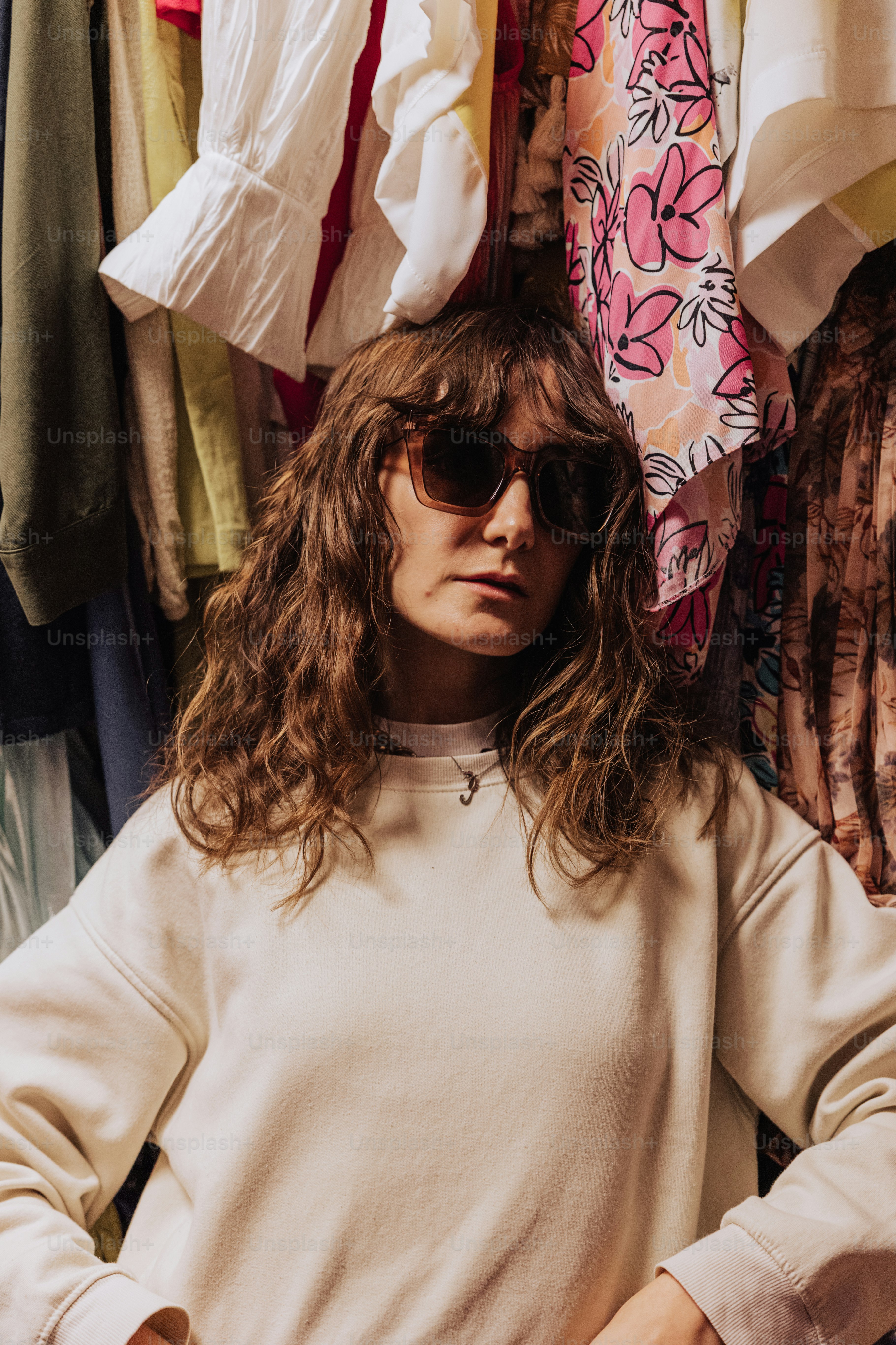 a woman wearing sunglasses standing in front of a rack of clothes