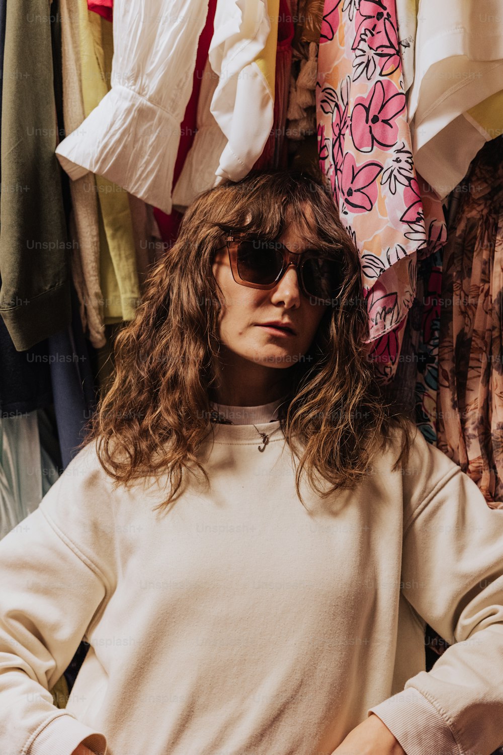 a woman wearing sunglasses standing in front of a rack of clothes