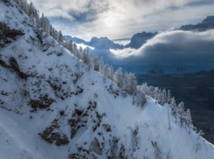 a snow covered mountain side with trees and clouds