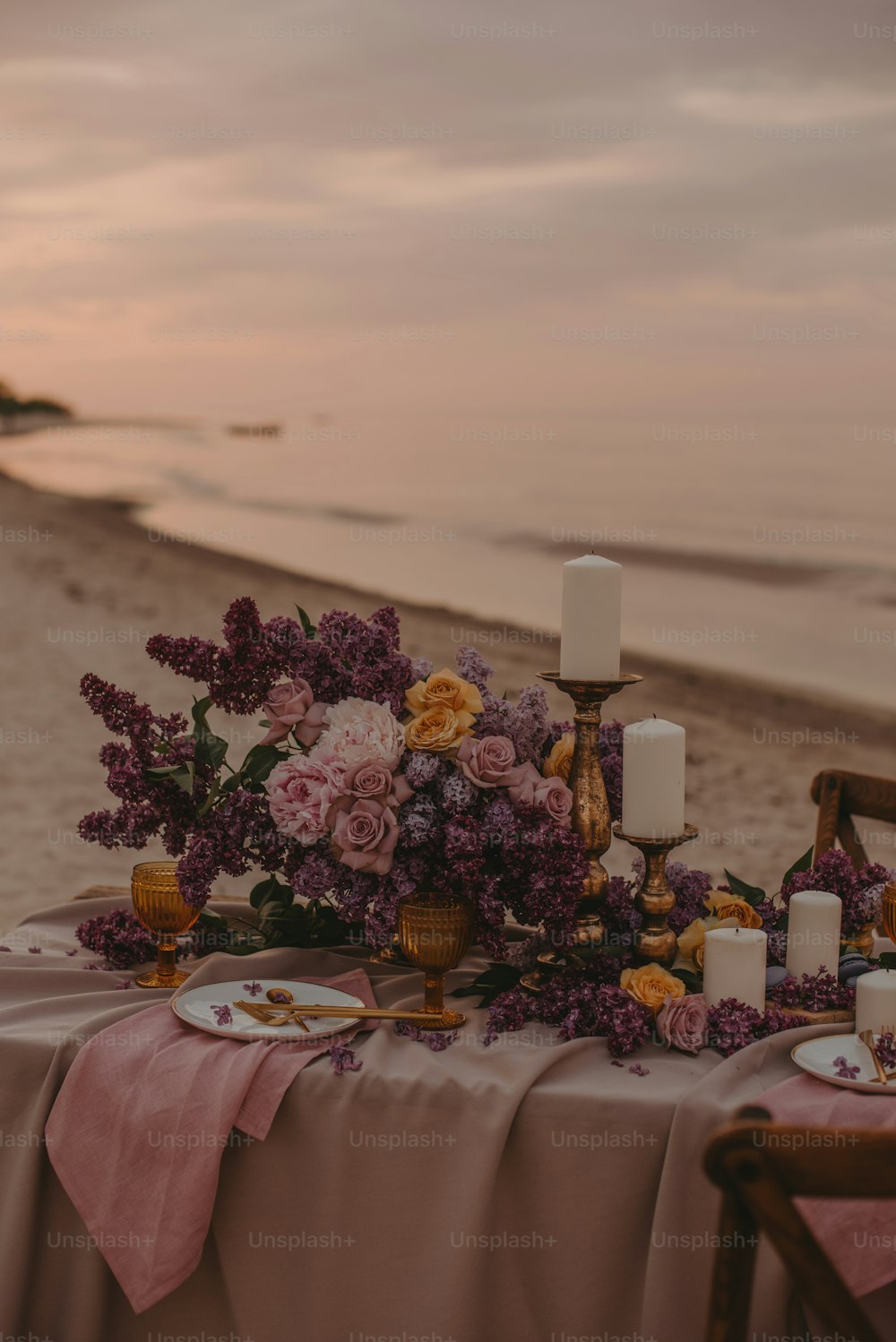 a table set up on the beach with flowers and candles