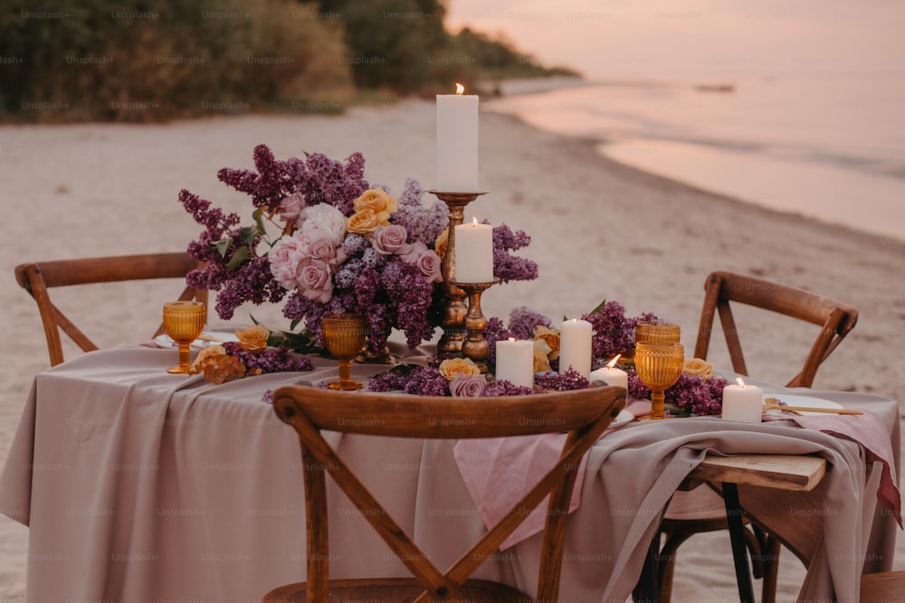 a table set up on the beach with flowers and candles