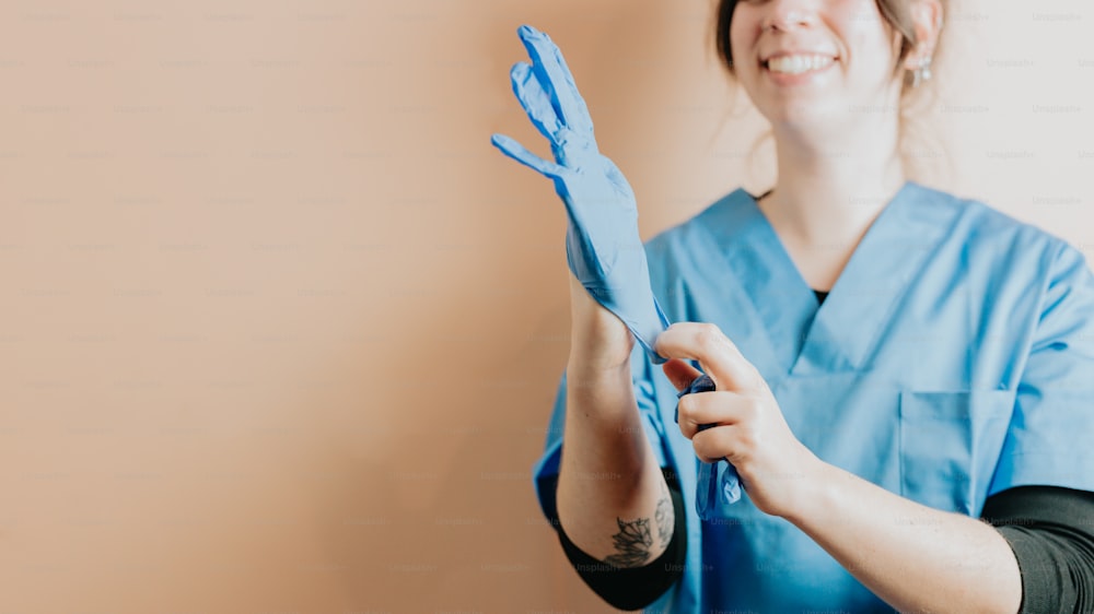 a woman in scrubs holding up a pair of blue gloves