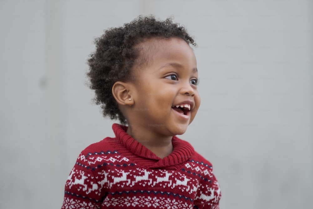 a young child smiles while wearing a red sweater