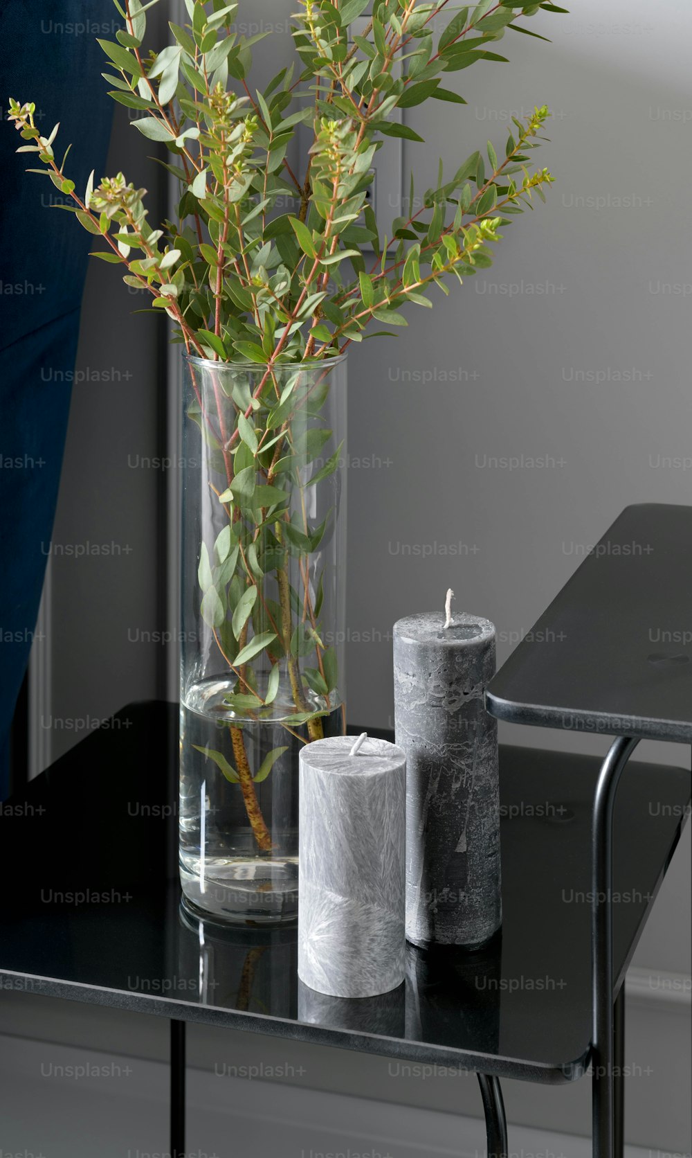 a glass vase with a plant and two candles on a table