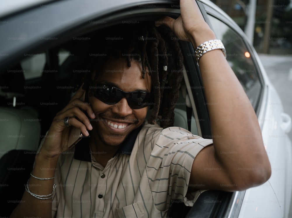 a man with dreadlocks sitting in a car talking on a cell phone