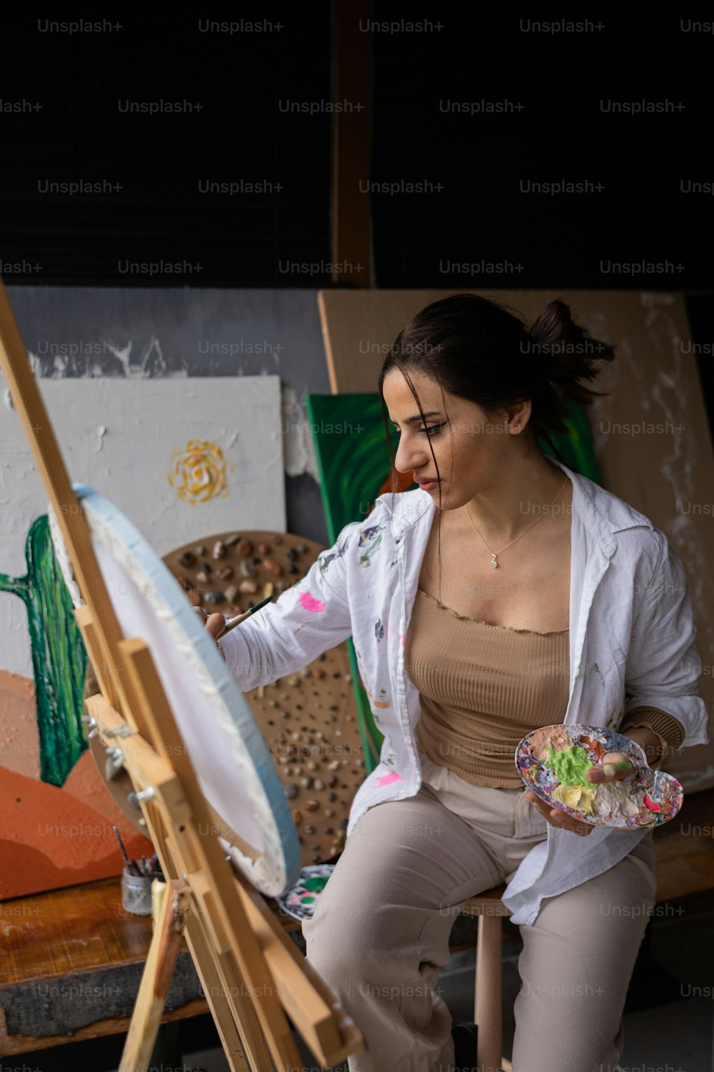 a woman sitting in front of a easel holding a plate of food
