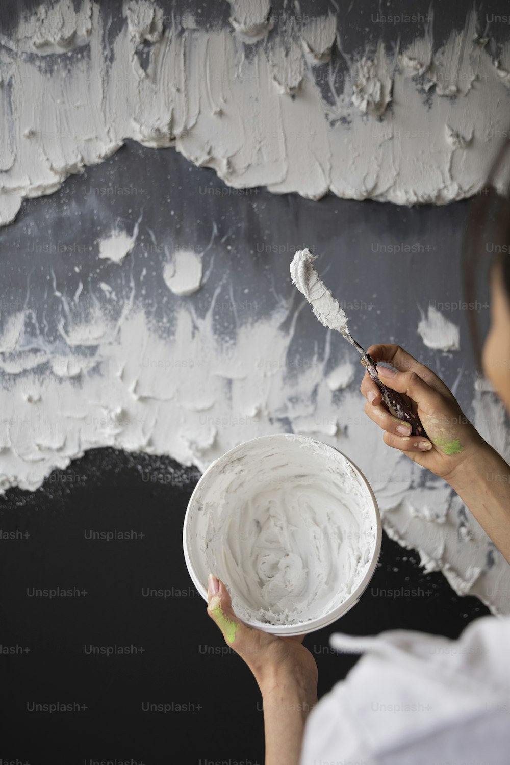 Une femme peint un mur avec de la peinture blanche