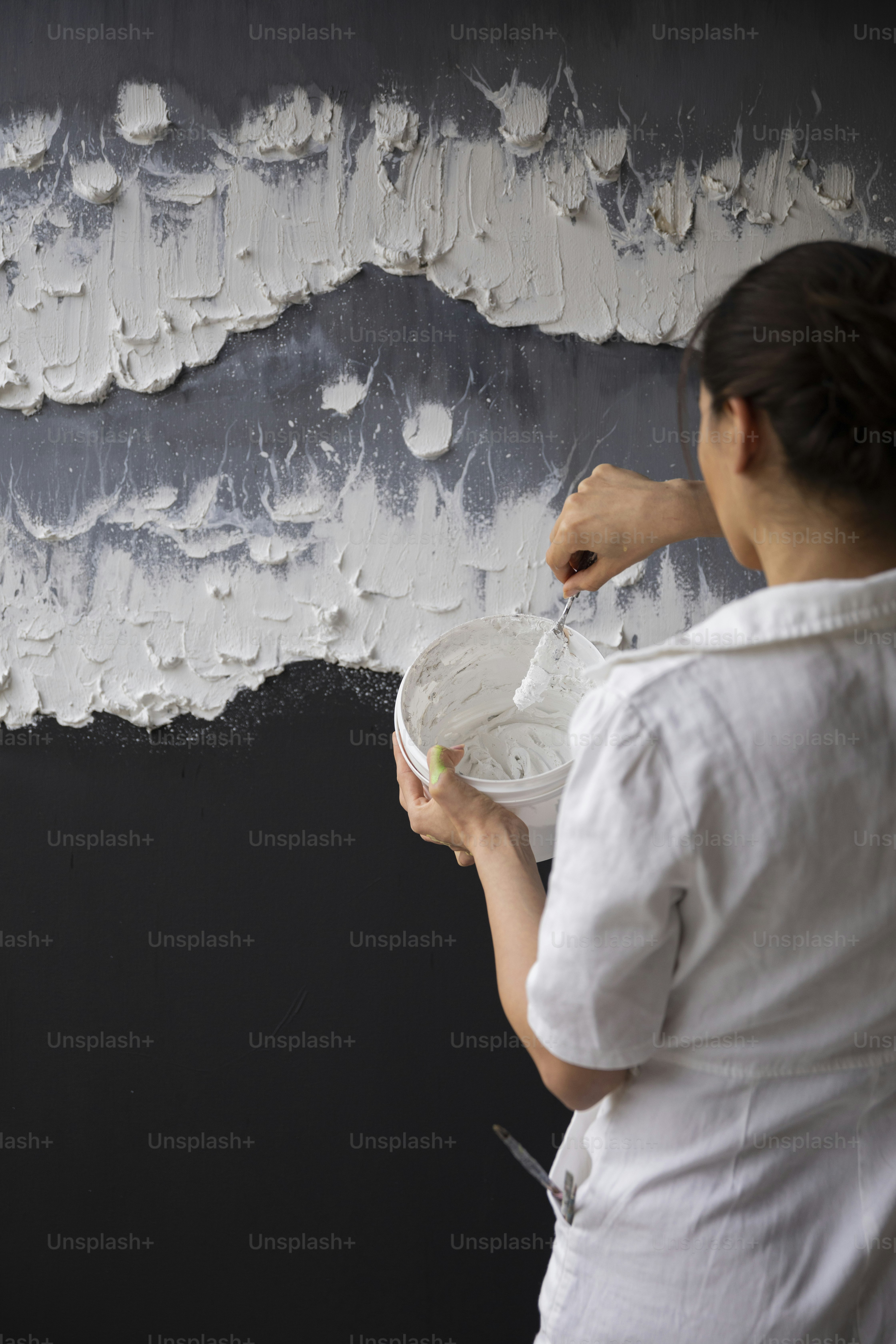 a woman painting a wall with white paint