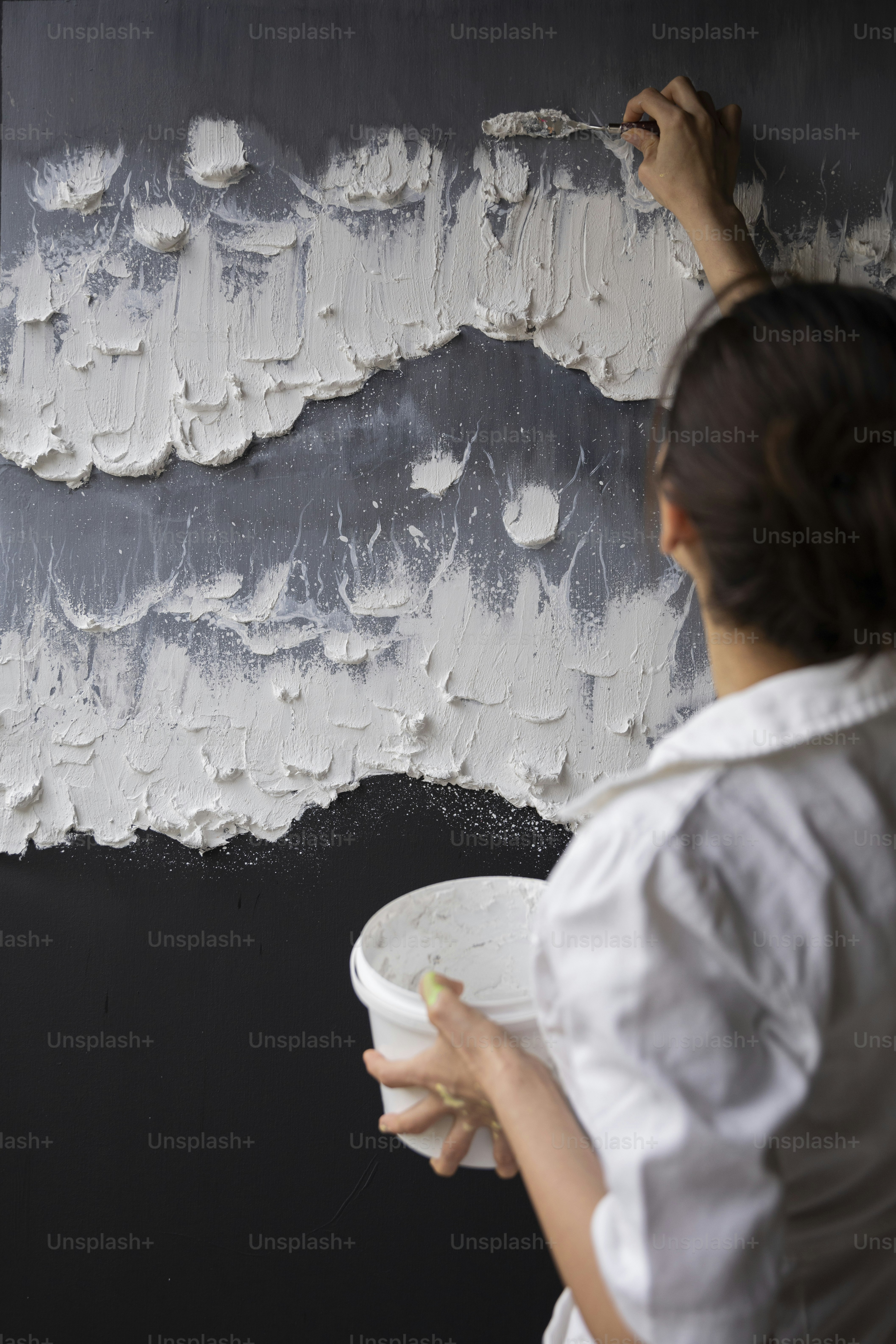 a woman painting a wall with white paint