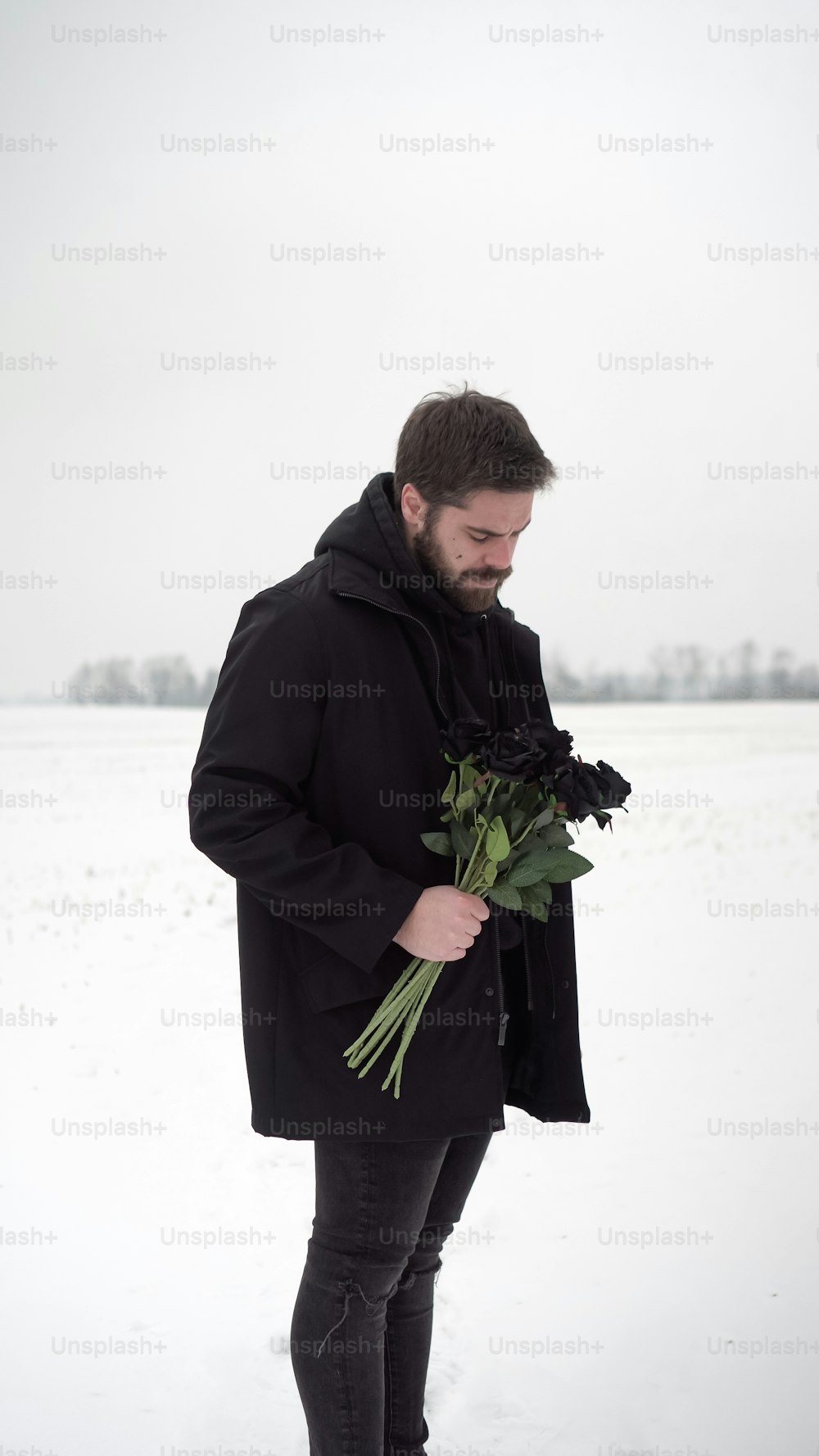 a man standing in the snow holding a bunch of flowers