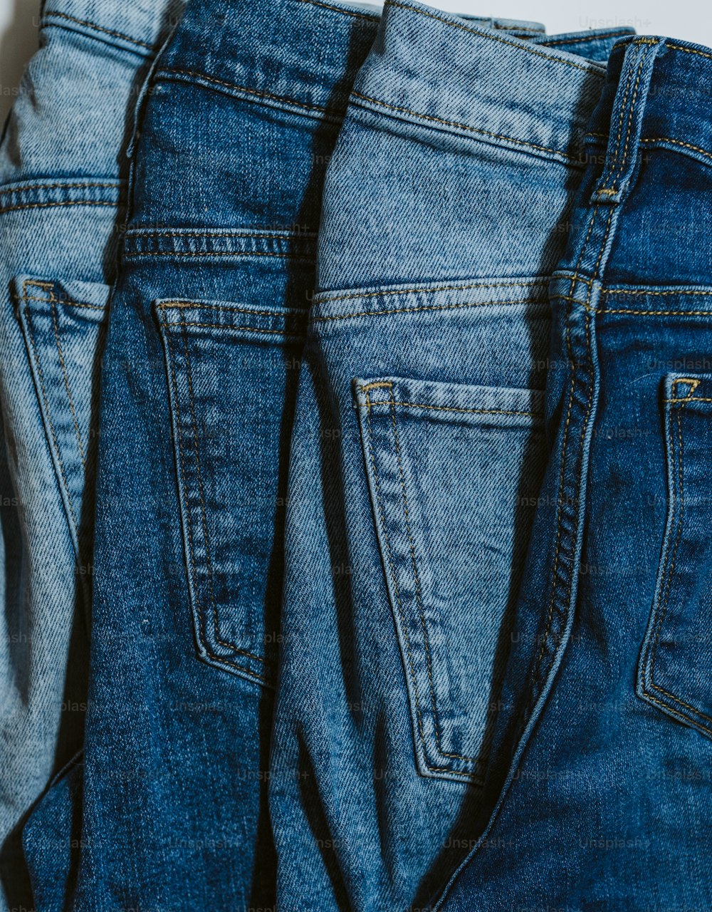 três pares de jeans estão alinhados em uma superfície branca
