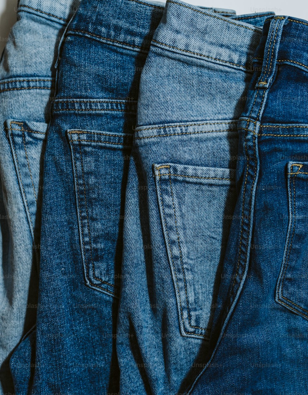 Tres pares de jeans están alineados sobre una superficie blanca