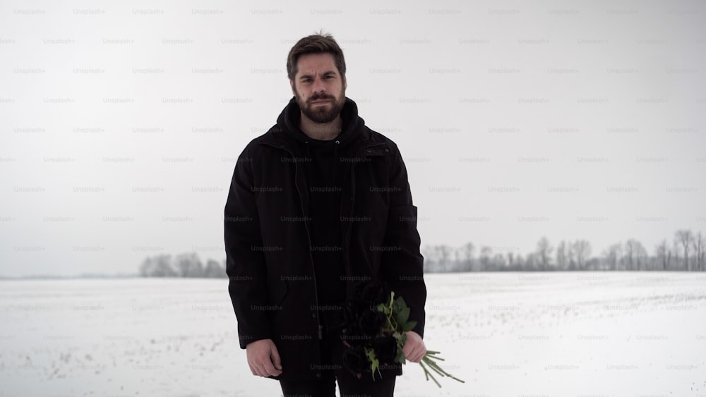 Un uomo in piedi nella neve con in mano un mazzo di fiori