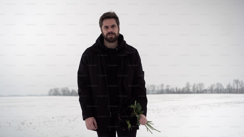 a man standing in the snow holding a bouquet of flowers