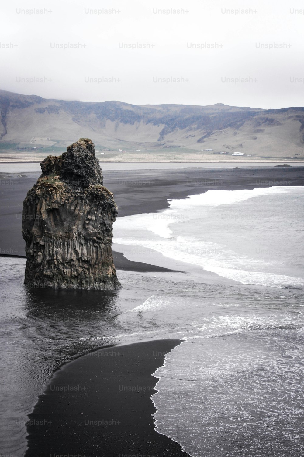 un gros rocher sortant de l’eau sur une plage
