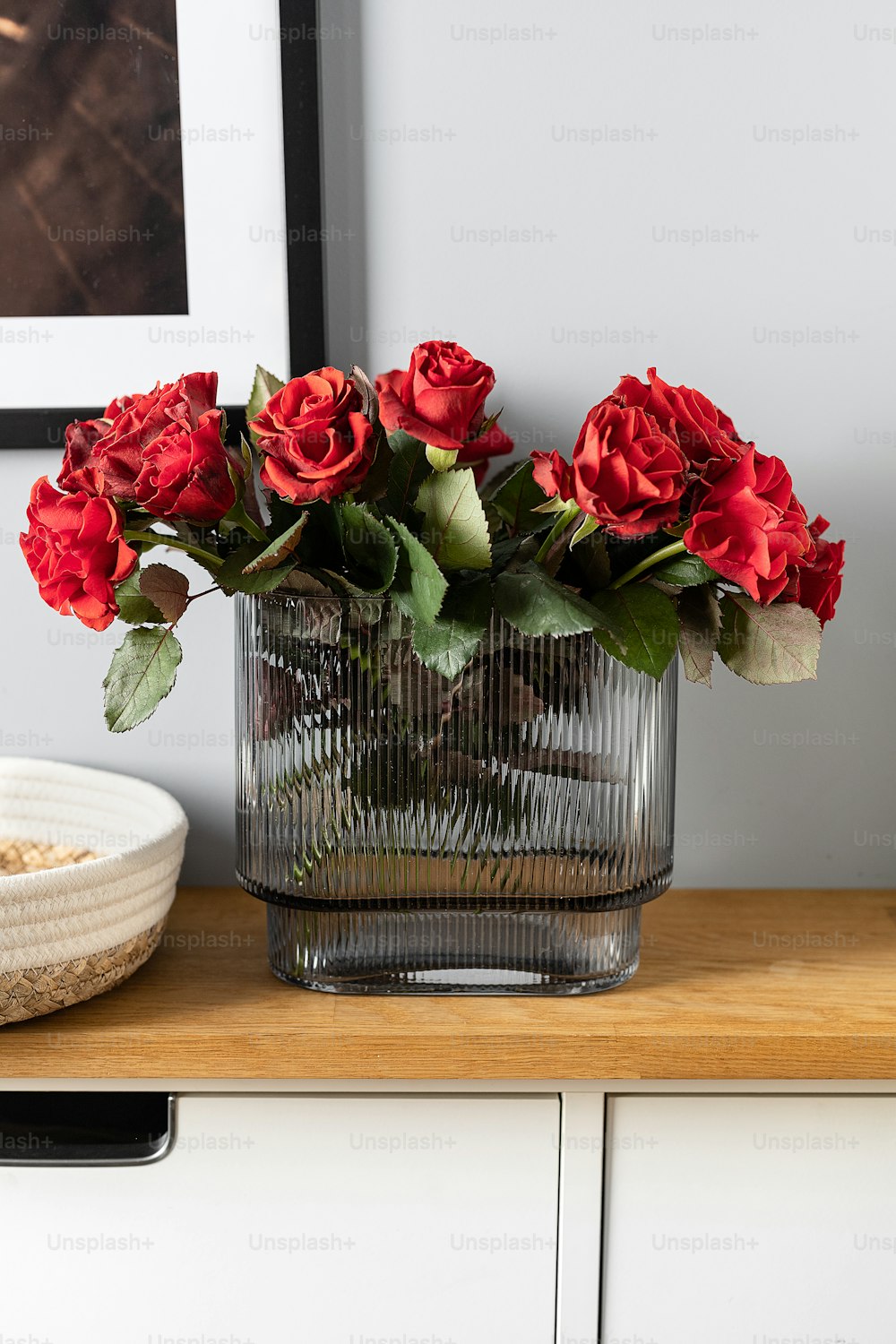 Un jarrón de vidrio lleno de rosas rojas encima de una mesa de madera