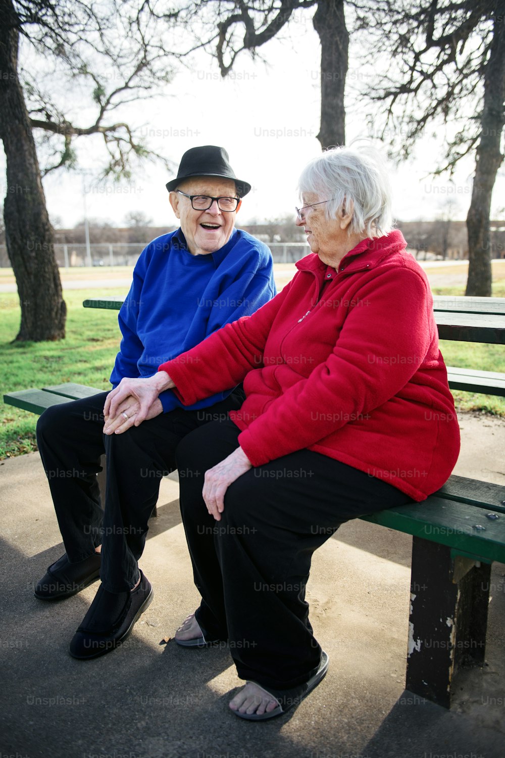 two elderly people sitting on a bench in a park