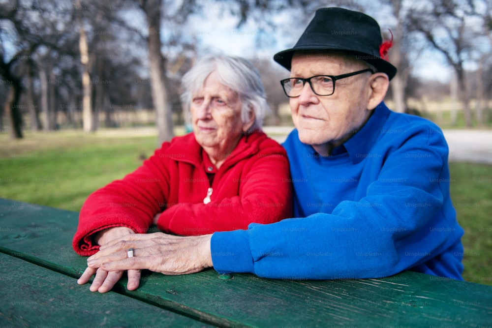 an elderly couple sitting on a bench in a park
