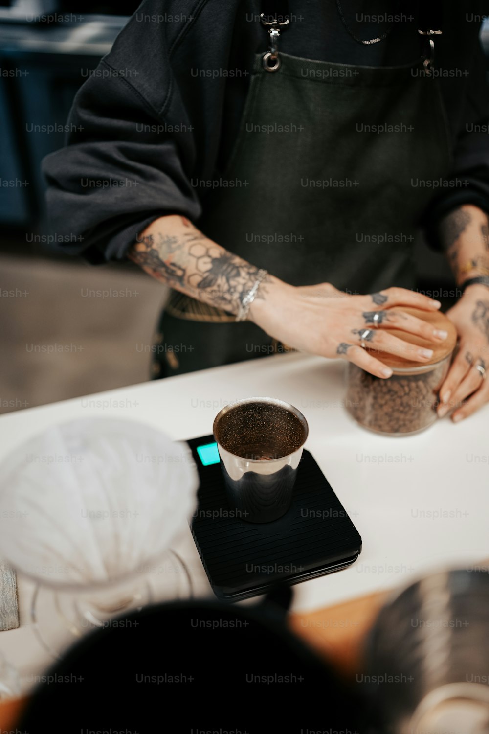 Un hombre con un tatuaje en el brazo está preparando una taza de café