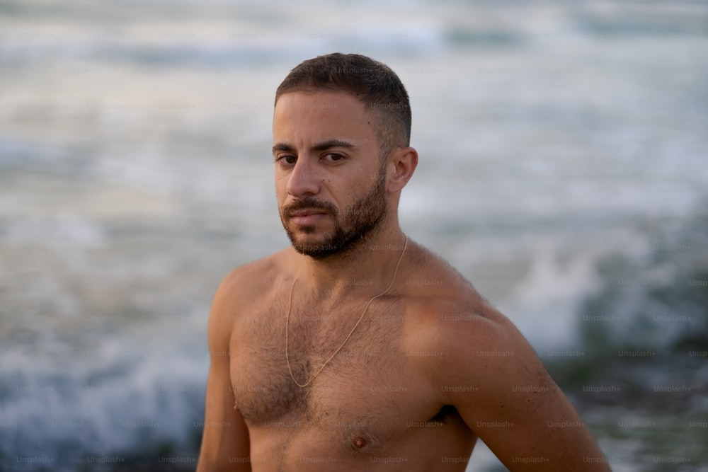 a man with no shirt standing in front of a body of water
