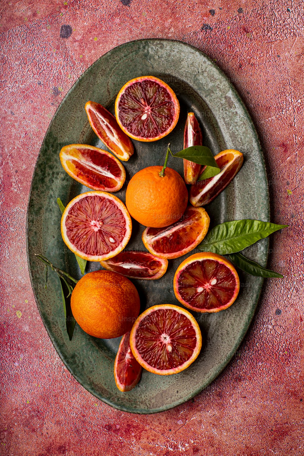 a plate of blood oranges with leaves on a table
