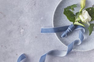 a white rose with a blue ribbon on a plate