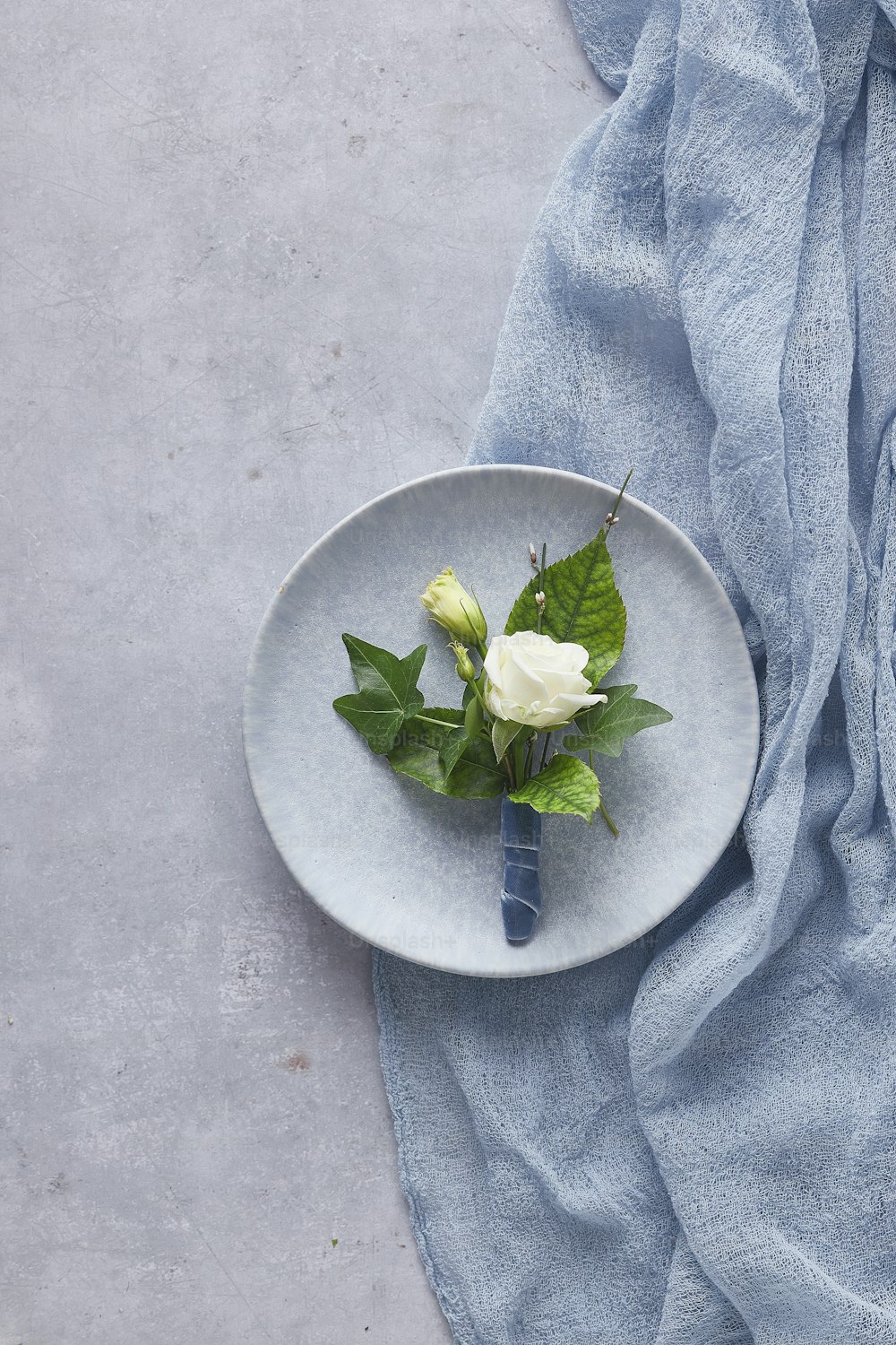 eine weiße Rose auf einem Teller auf einem blauen Tuch