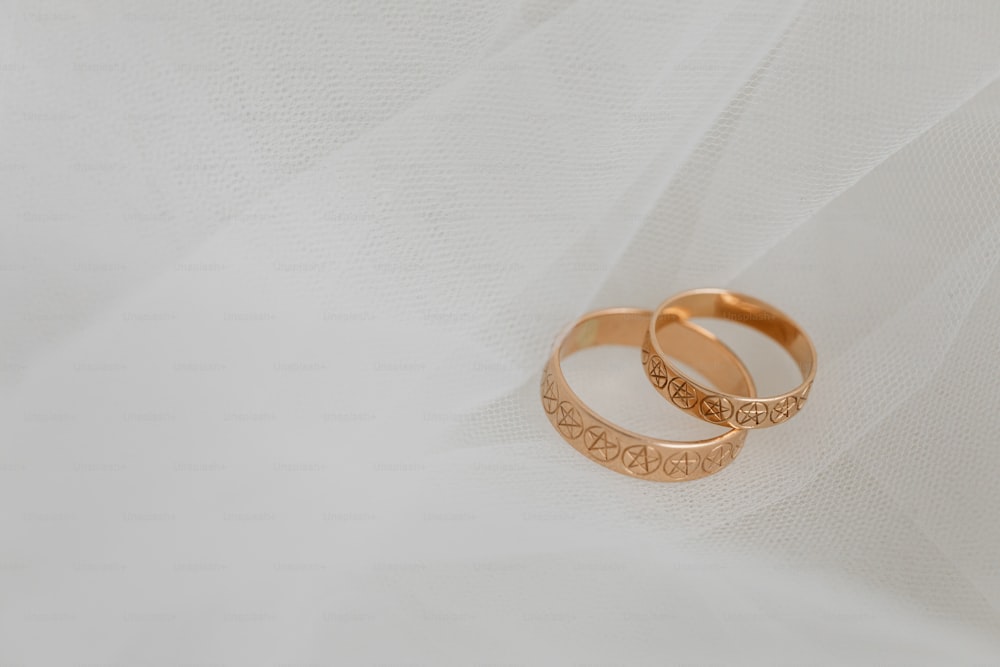 two gold wedding rings sitting on top of a white cloth