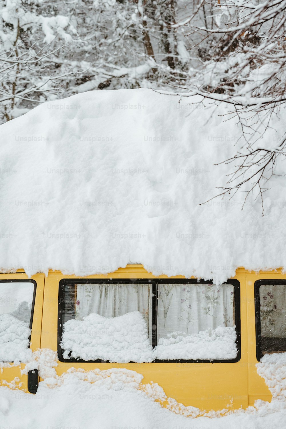 a yellow bus covered in snow next to trees