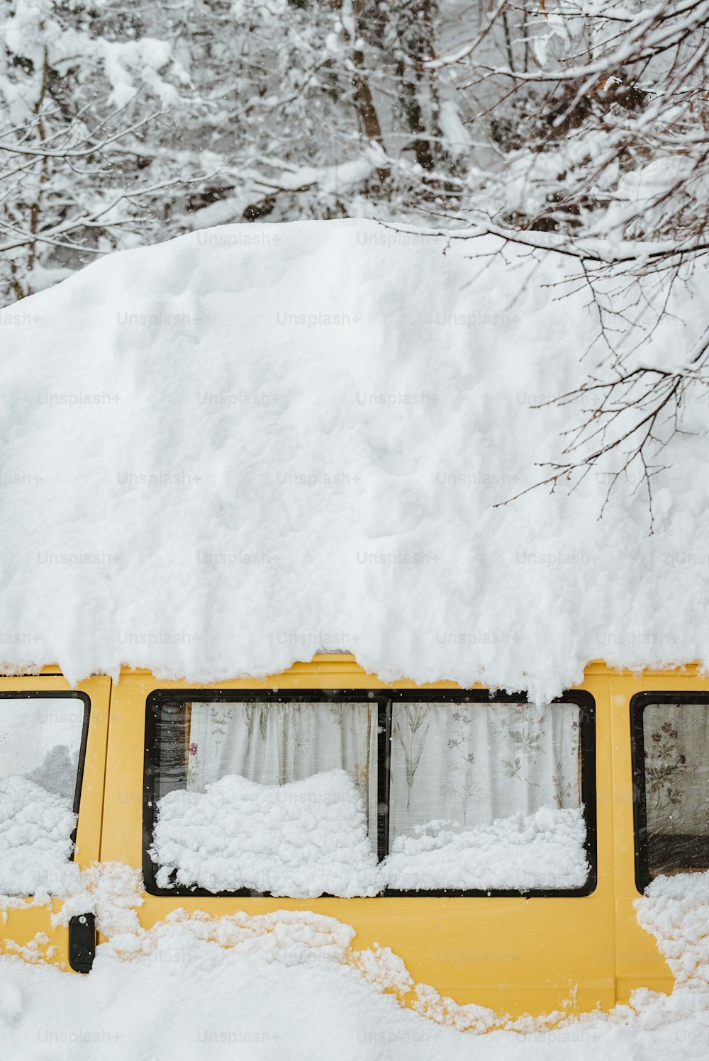 a yellow bus covered in snow next to trees