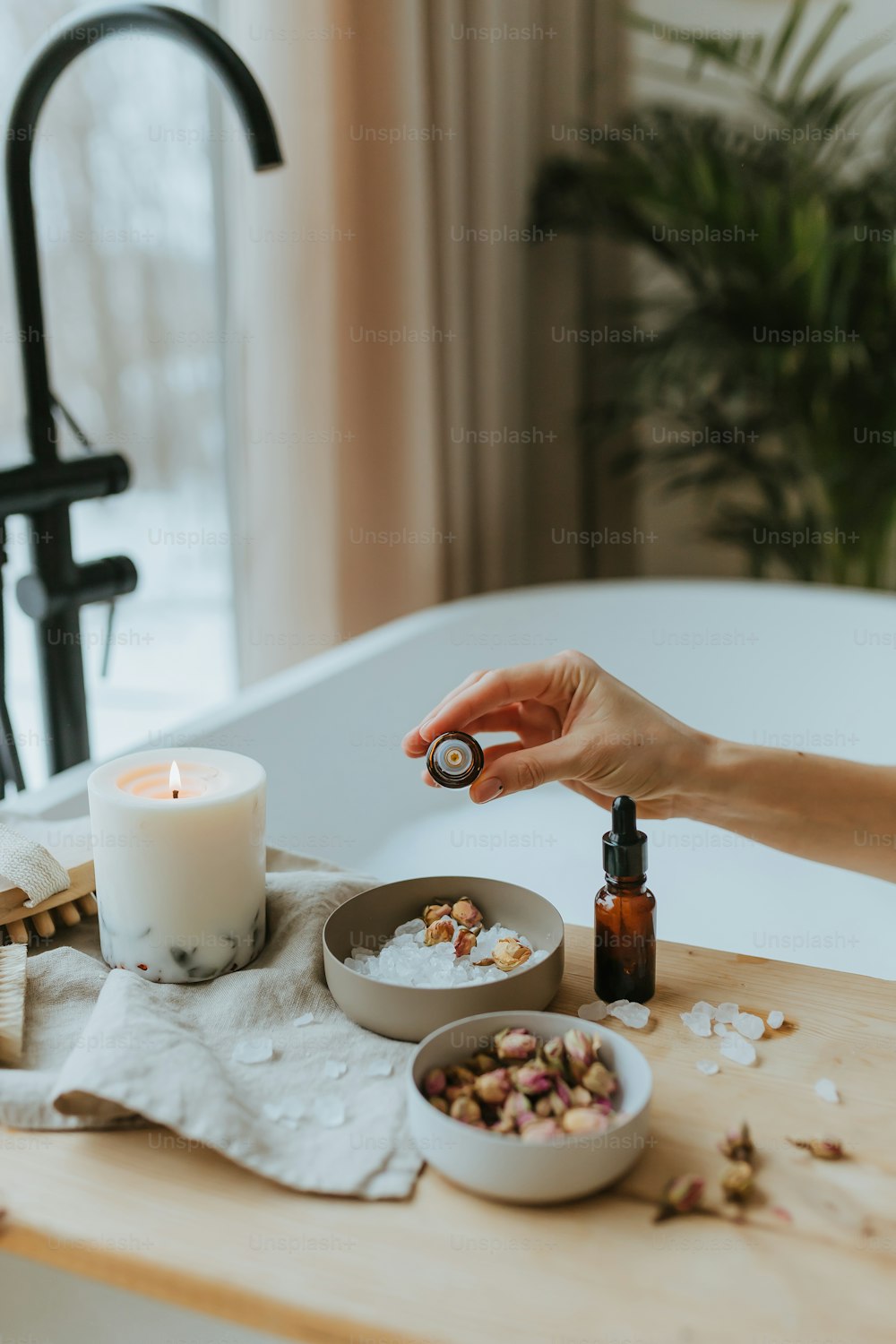 a person holding a bottle of essential oils near a bathtub