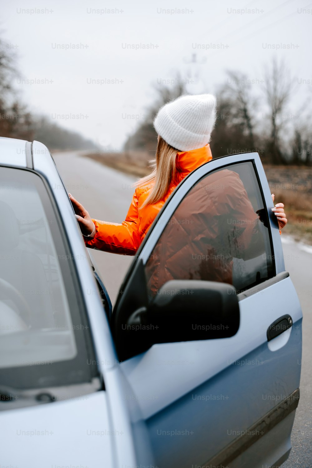 a woman in an orange jacket leaning out of a car window