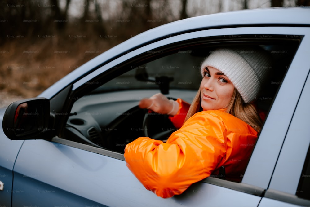 a woman in an orange jacket driving a blue car