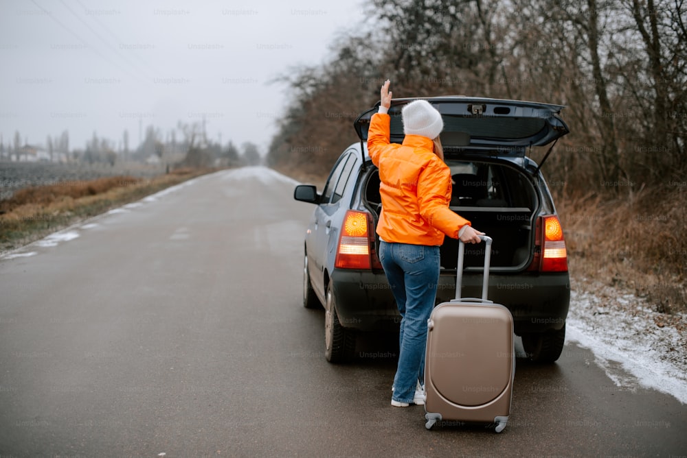 Une femme en veste orange tient une valise