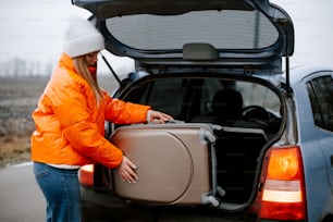 a woman loading a suitcase into the back of a car