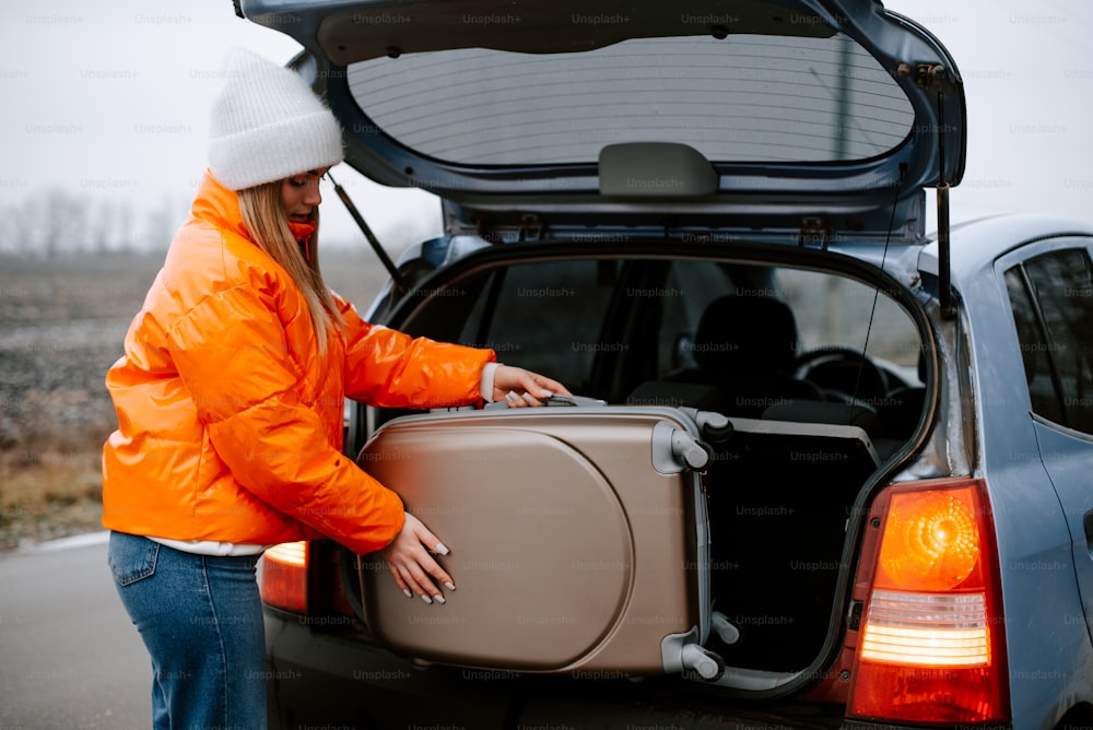a woman loading a suitcase into the back of a car