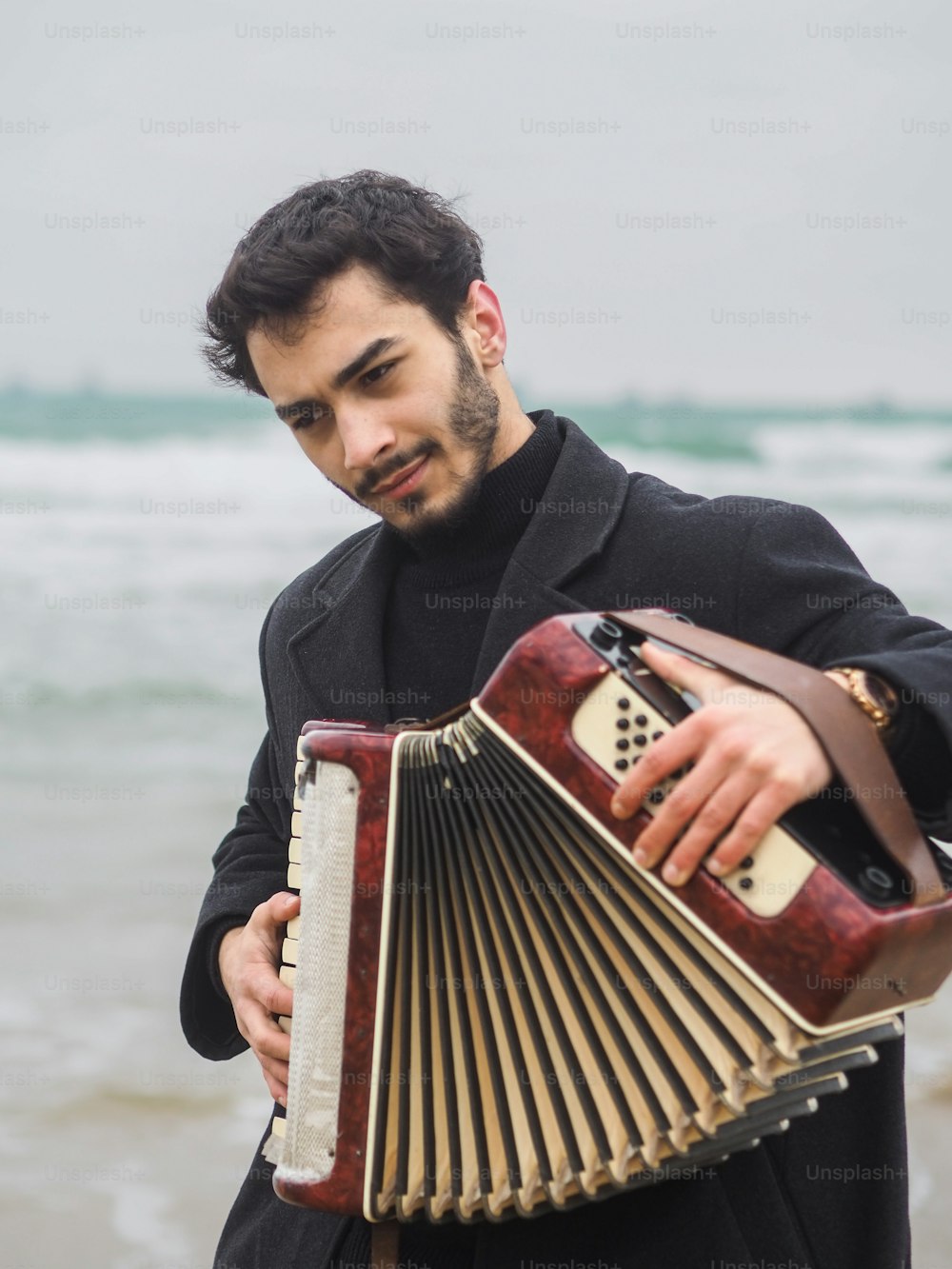 a man holding an accordion in front of the ocean
