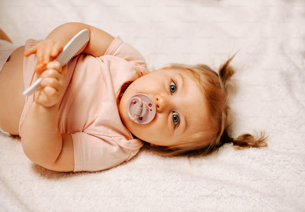 a baby laying on a bed with a toothbrush in her mouth