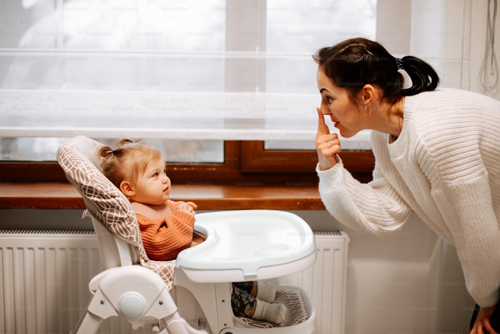 a woman brushing her teeth next to a baby in a high chair